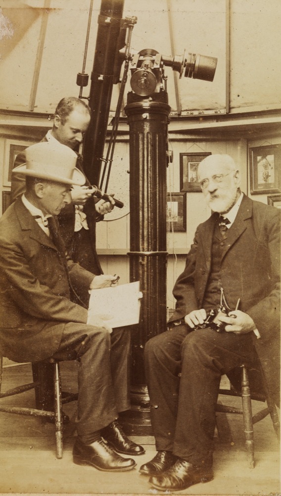Une lunette astronomique ancienne sur sa monture dans une coupole, avec trois hommes assis autour