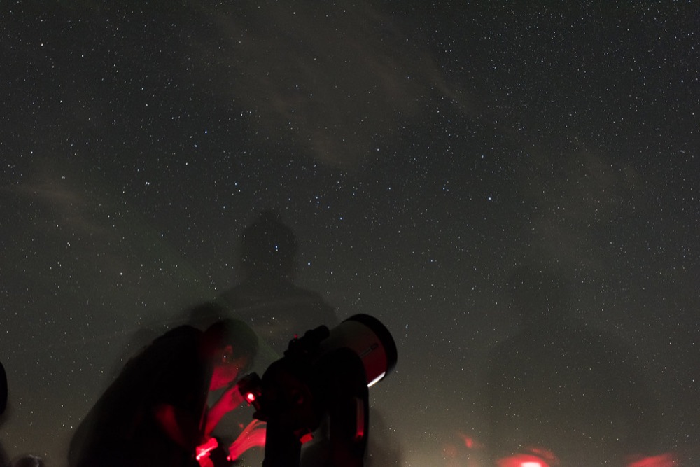 Un observateur penché sur son instrument d'astronomie sous un ciel étoilé, comme pour une lunette astronomique