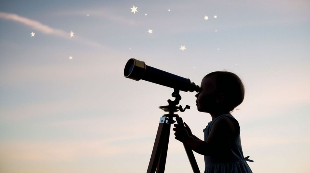 Enfant qui observe le ciel étoilé avec un télescope installé dans le jardin